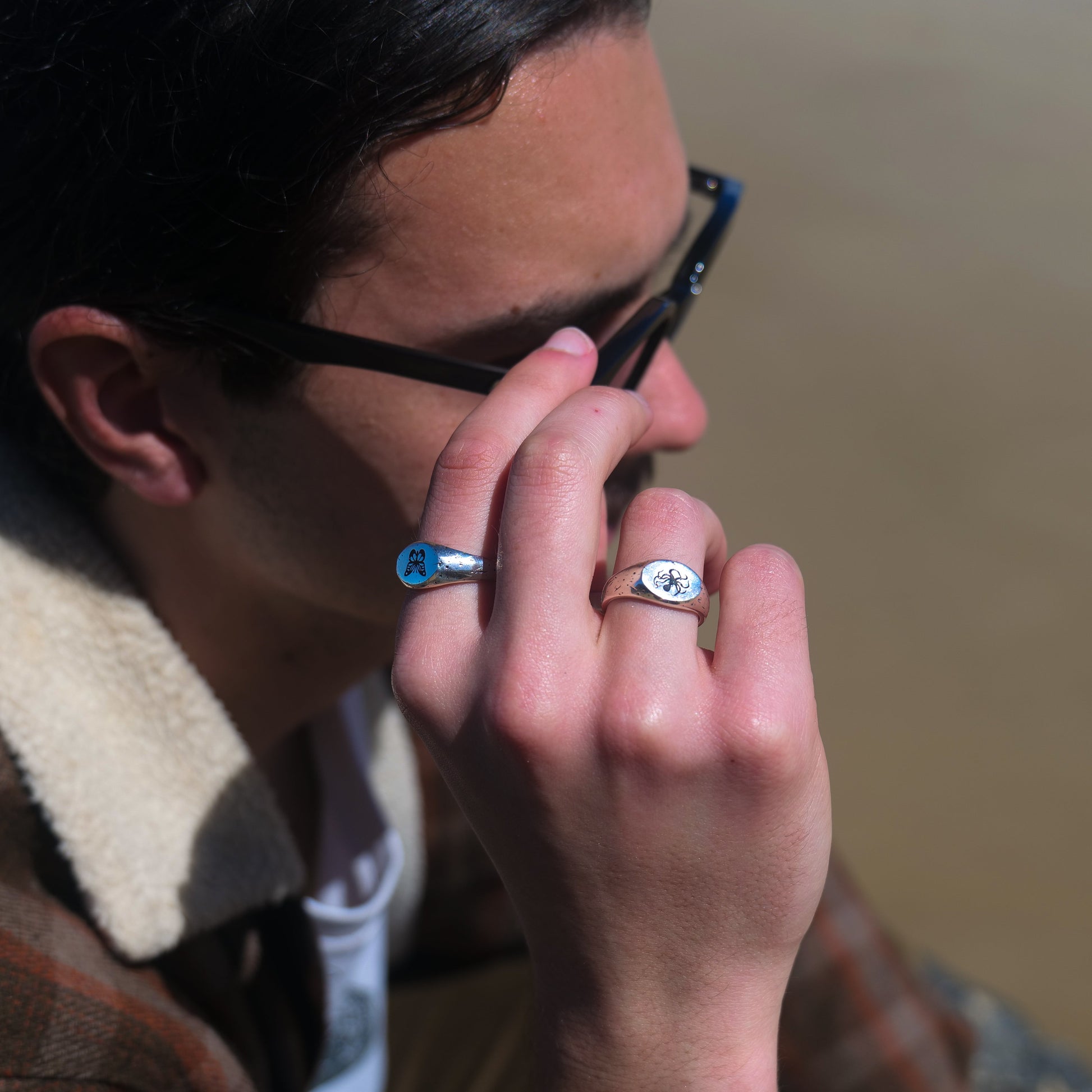Man holding glasses wearing butterfly + kraken rings.