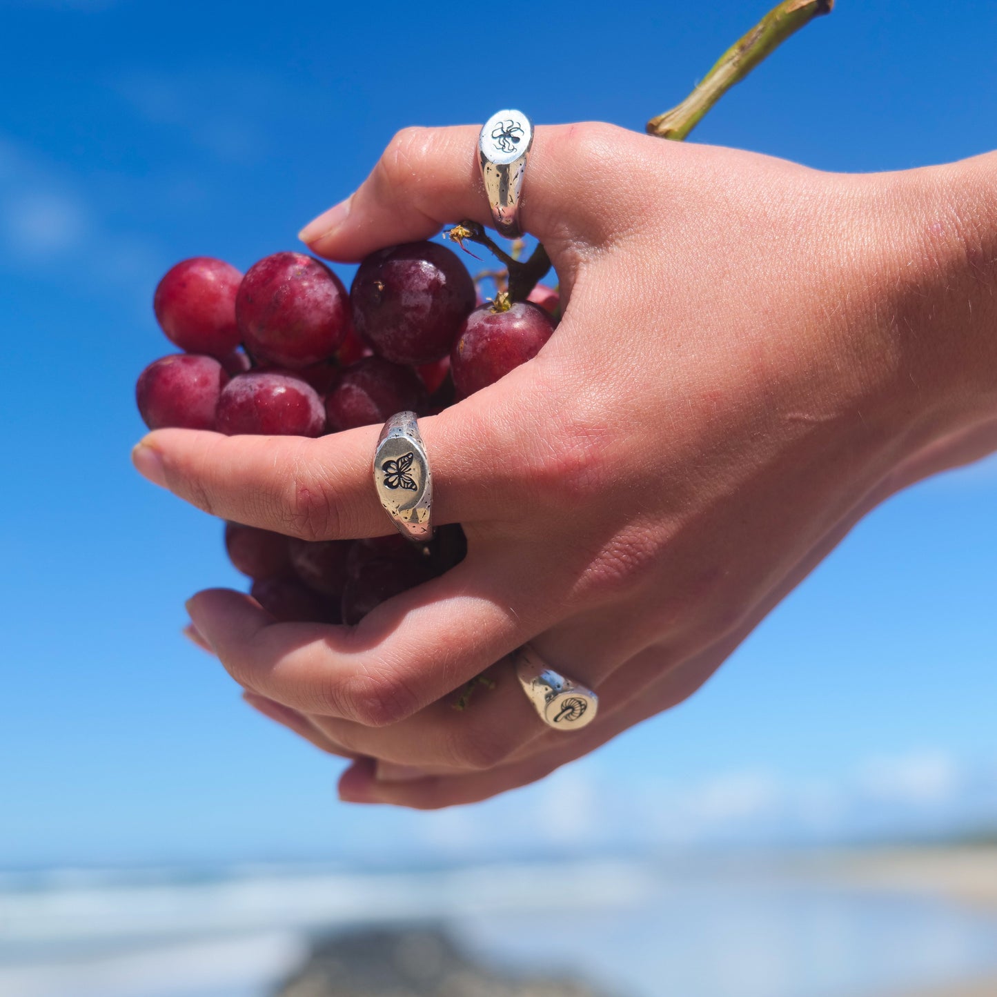Woman holding grapes wearing kraken + butterfly + mushy rings.