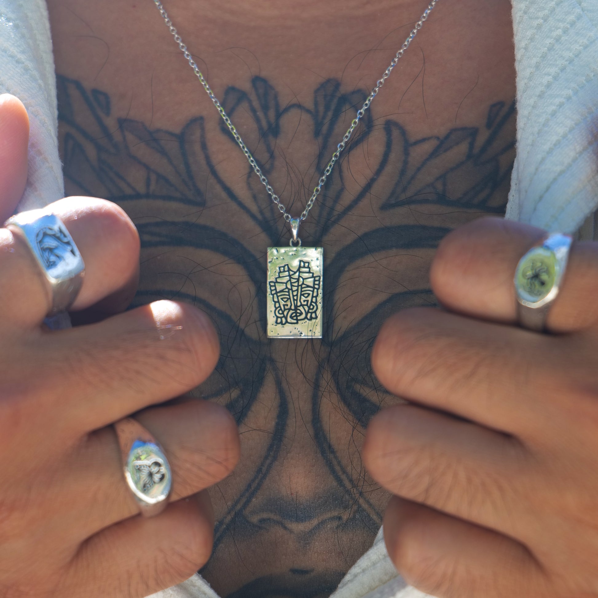 Man with chest tattoo wearing serpent + butterfly + kraken rings + Aztec pendant.