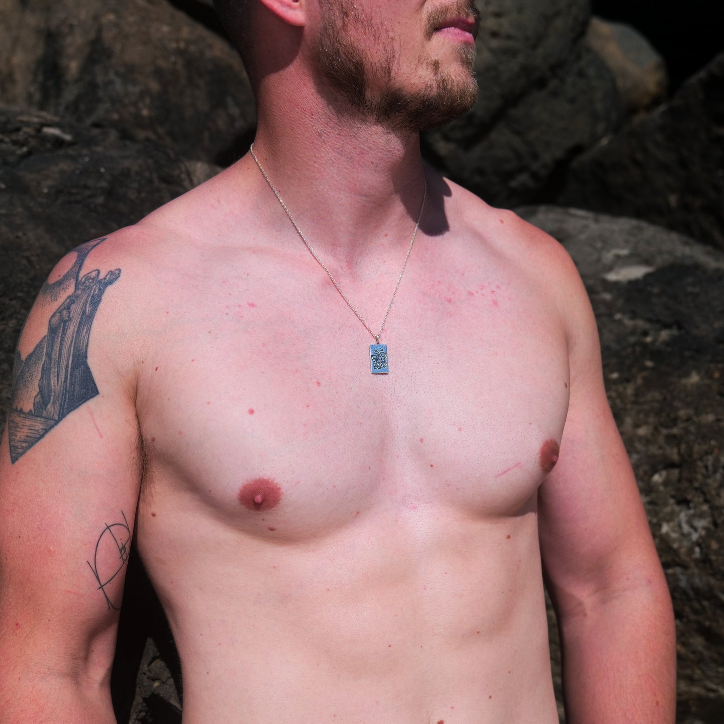 Man with shoulder and bicep tattoo wearing Aztec pendant.
