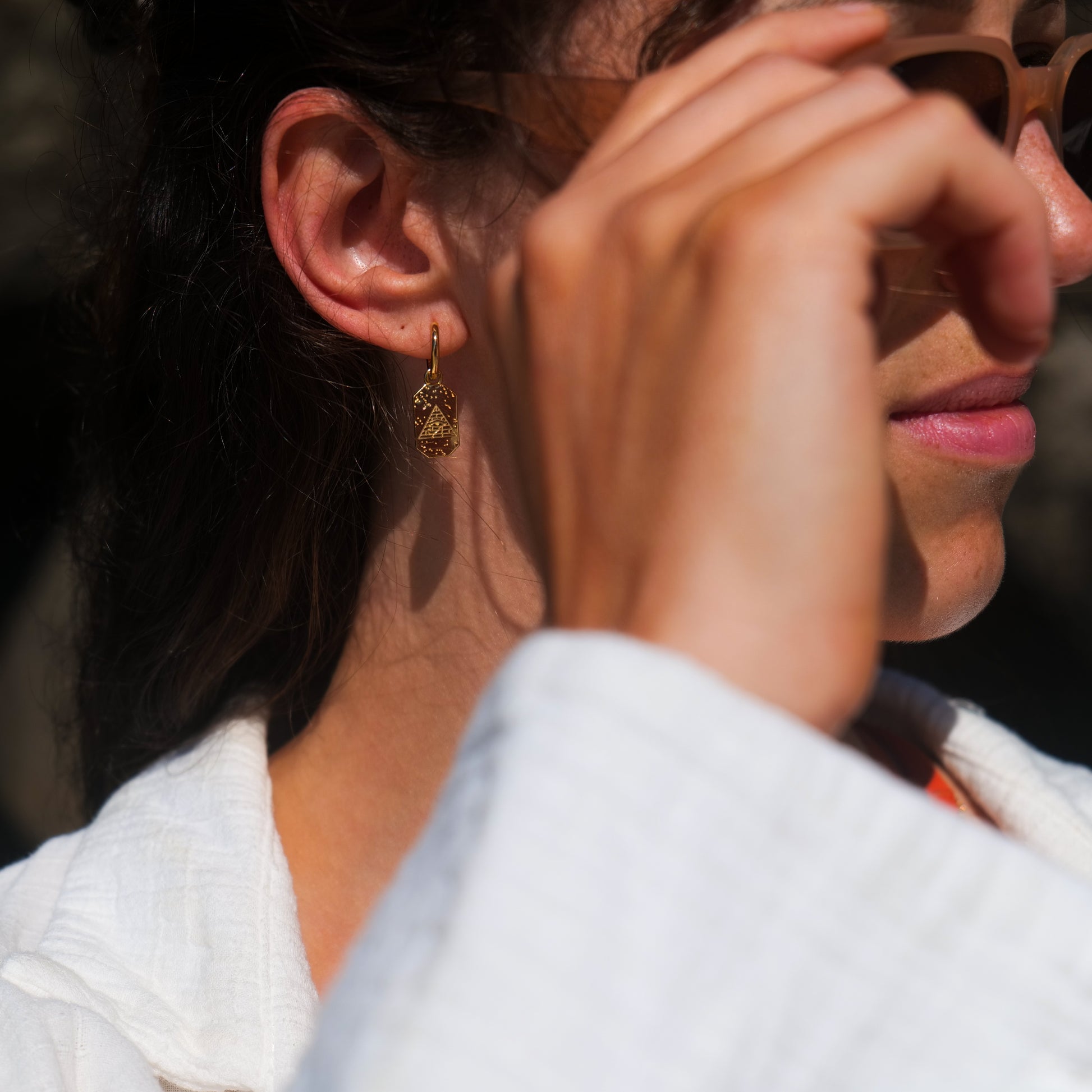 Woman holding glasses wearing eye of Ra earring.